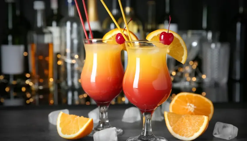 Dwa drinki z wódką czystą, ozdobione pomarańczą i wiśnią, z kostkami lodu i owocami w tle.