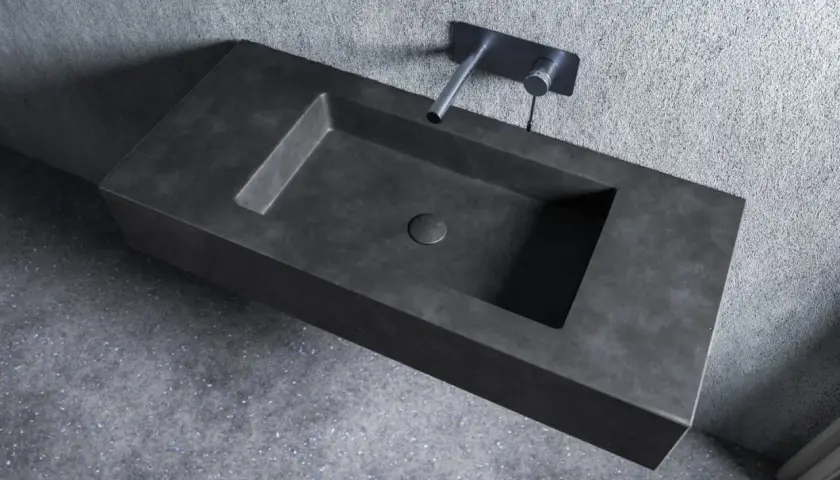 Nowoczesna umywalka z betonu o minimalistycznym designie, z wpuszczonym w blat odpływem i elegancką baterią ścienną.