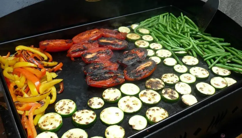 Poivrons, tomates, courgettes et haricots verts grillés sur une plancha. Une délicieuse pierrade végétarienne en préparation.
