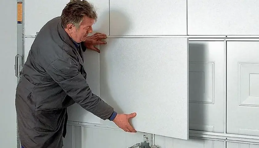 Mężczyzna montuje panel do ocieplenia bramy garażowej segmentowej.