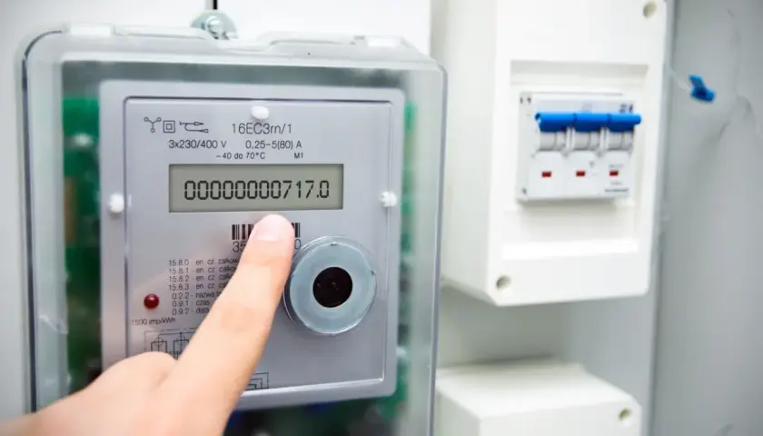Palec wskazuje licznik prądu, pokazując jak odczytać jego wskazania. Cyfrowy wyświetlacz pokazuje zużycie energii.