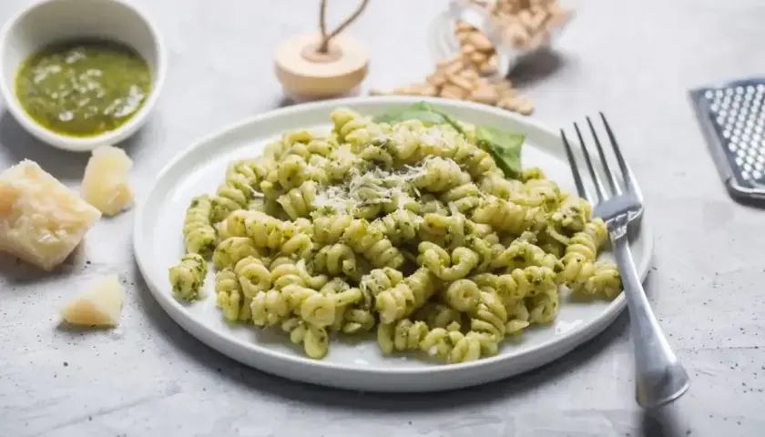 Pyszny makaron z pesto, posypany parmezanem, z dodatkiem świeżej bazylii i orzeszków piniowych.