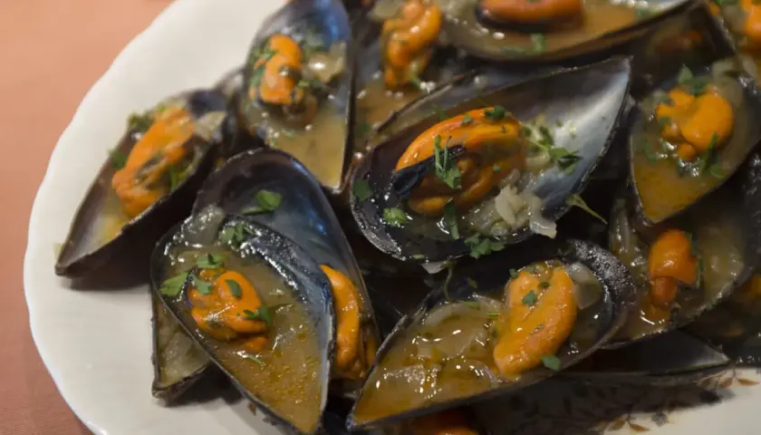 Un plato lleno de mejillones a la marinera, jugosos y con perejil picado, listos para disfrutar.