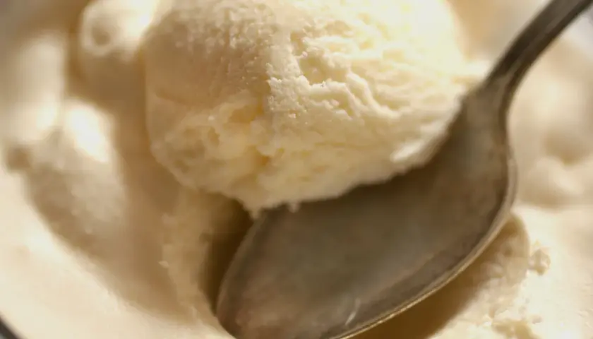 Kremowe lody z serka wiejskiego, idealne na deser. Łyżeczka zanurzona w słodkiej masie.