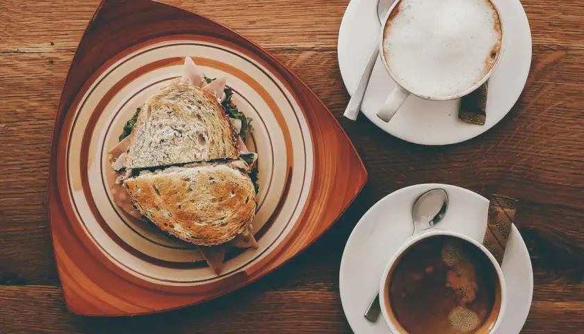 Ein Sandwich und ein Café Americano auf einem Holztisch.