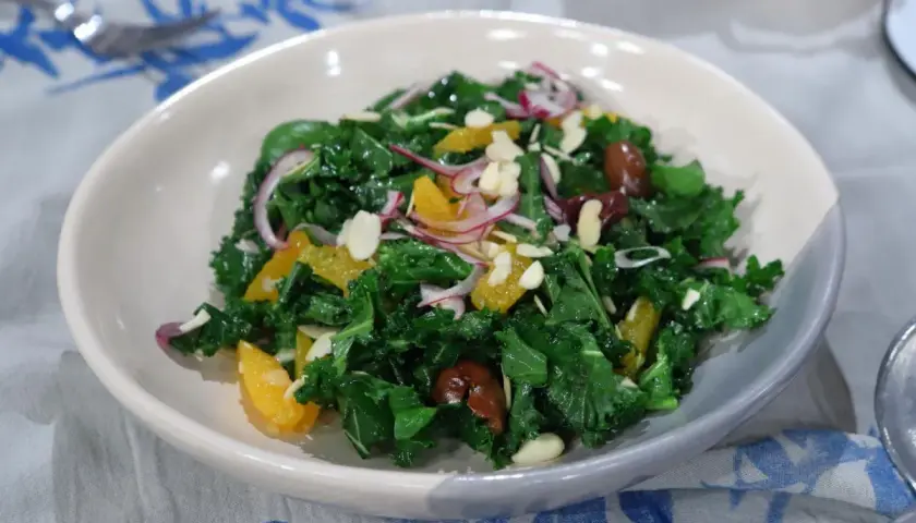 Ensalada siciliana vibrante con col rizada, gajos de naranja, cebolla morada, aceitunas y almendras laminadas.