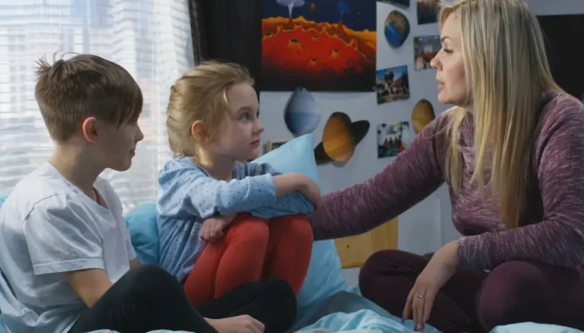 Kobieta z dwójką dzieci, otoczona plakatami kosmicznymi, rozmawia o przyczyny popularności motywu "found family" w literaturze przygodowej.