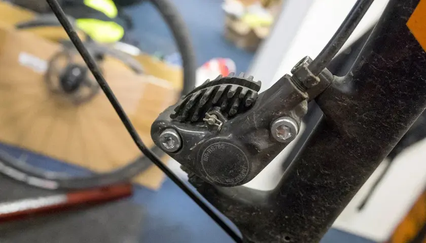 Close-up of a bicycle's hydraulic disc brake caliper, showing the brake fluid top and cooling fins.
