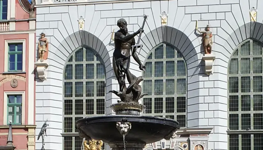 Fontanna Neptuna znajduje się w Gdańsku, przed fasadą budynku z arkadowymi oknami. Rzeźba przedstawia boga mórz na tle kamiennej architektury.