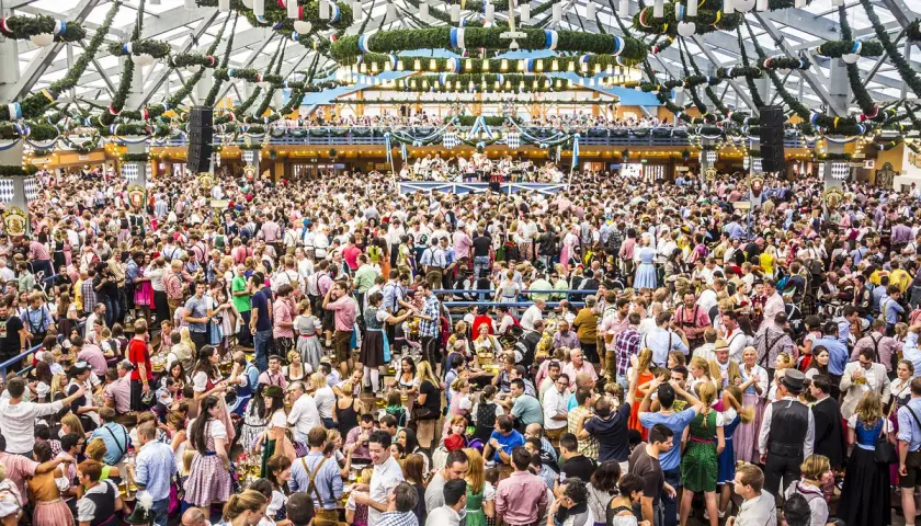Riesiges Festzelt voller Menschen in Tracht. Die Frage "wie lang geht die Wiesn" beschäftigt viele Besucher dieses Volksfestes.