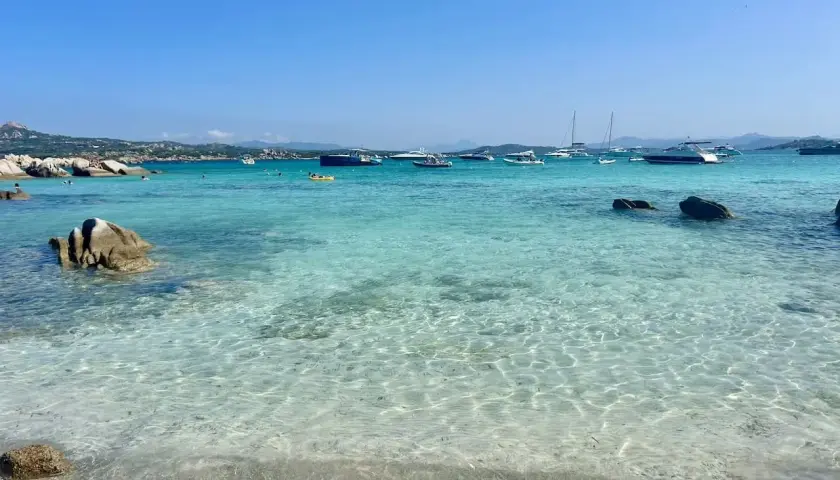 Plage de rêve en Sardaigne, eaux turquoise cristallines, rochers, bateaux au mouillage. Un coin de paradis pour savourer la ciaccia sarde.