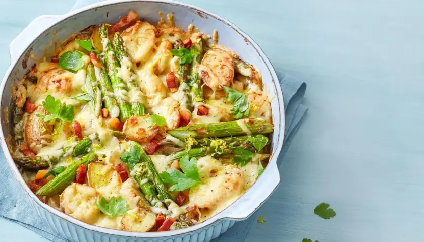 Herzhafter Spargel Auflauf mit Kartoffeln, Speck und geschmolzenem Käse, garniert mit Petersilie und Zitronenschale.