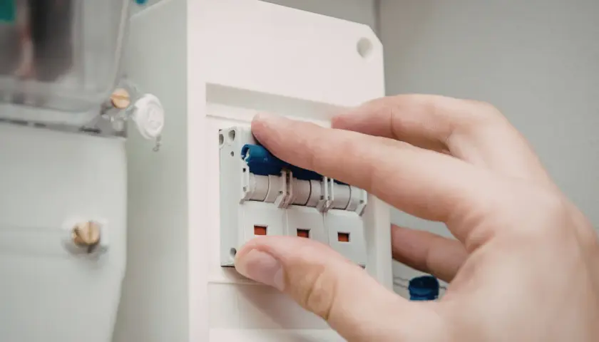 Dłoń manipuluje wyłącznikami w skrzynce elektrycznej. Dowiedz się, jak dobrać zabezpieczenie prądowe.