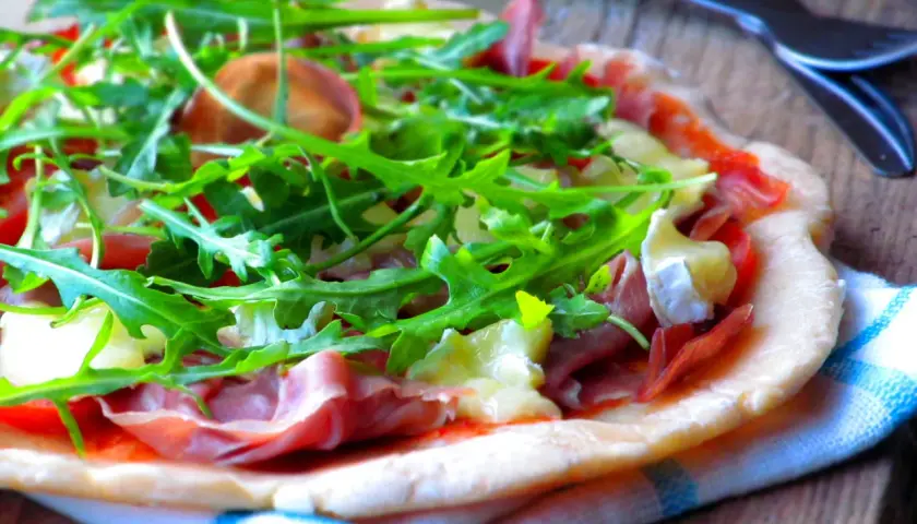 Pyszna pizza parma z rukolą i serem pleśniowym, gotowa do pokrojenia.