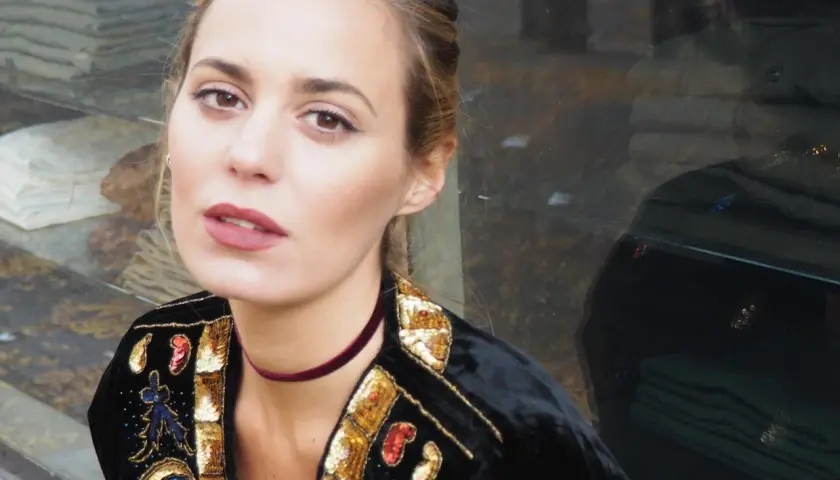 Claudia Ortiz Domecq, con un choker de terciopelo y chaqueta bordada, posa con mirada intensa frente a un escaparate.