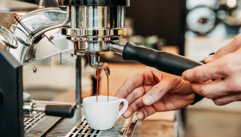 Frisch gebrühter Espresso fließt aus der Maschine in eine kleine Tasse. Die Zubereitung von handgebrühtem Kaffee ist ein Kunstwerk.
