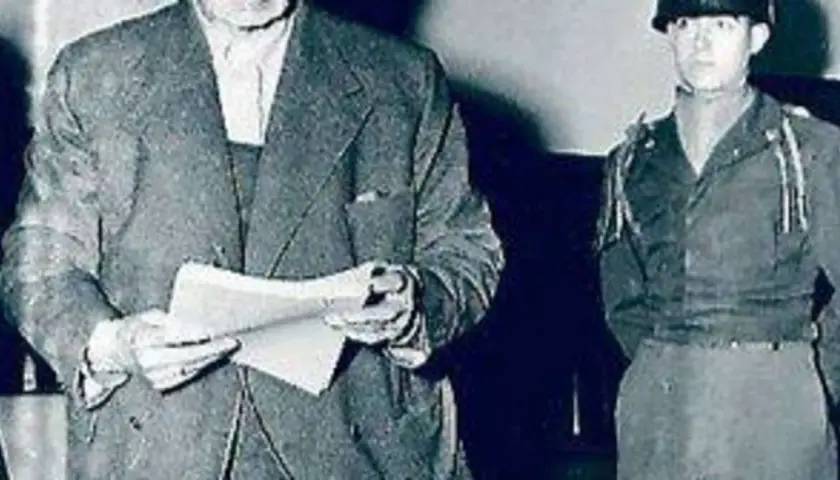 Ein Mann im Anzug hält Dokumente, daneben ein Soldat. Möglicherweise im Zusammenhang mit dem Flick-Konzern.