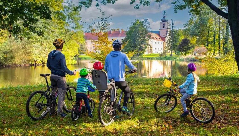 Rodzina na rowerach podziwia jesienny krajobraz krainy Górnej Odry. W tle pałac i jezioro.