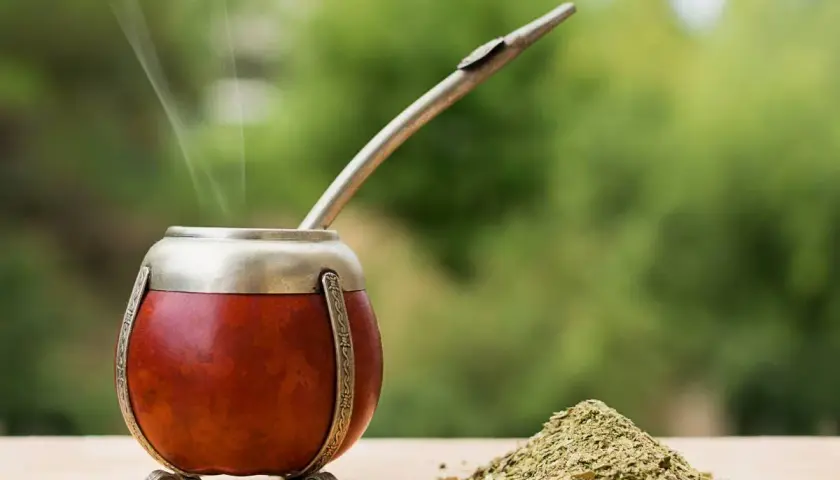 Parząca yerba mate Guarani w tykwie, z metalową bombillą i górką suszu na drewnianym blacie.