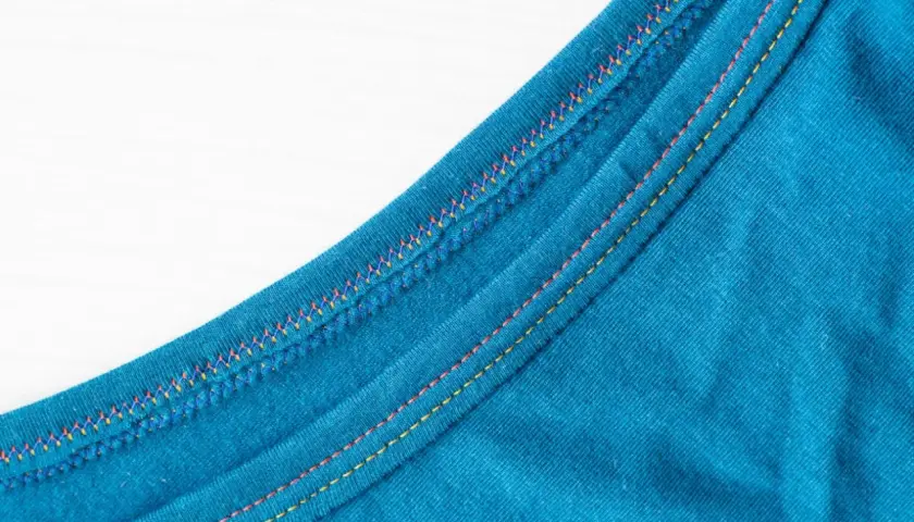 Close-up of teal fabric showing a decorative double needle topstitch with colorful threads, adding a vibrant detail to the garment's edge.