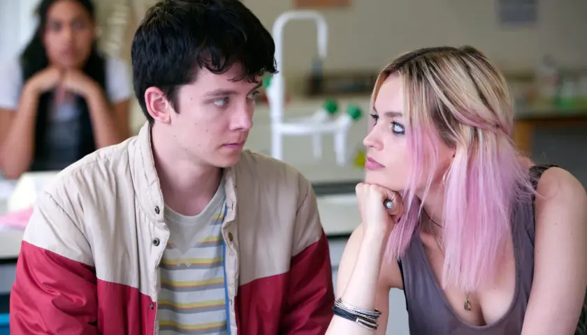 Una recensione di Sex Education: Otis e Maeve si guardano intensamente, mentre un'altra ragazza è sfocata sullo sfondo.