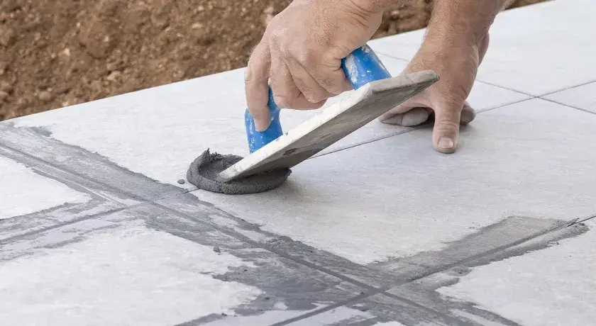 Hand arbeitet mit Spachtel, um graue Masse in Fliesenfugen zu verteilen. Präzises fliesenfugen abdichten für ein perfektes Ergebnis.