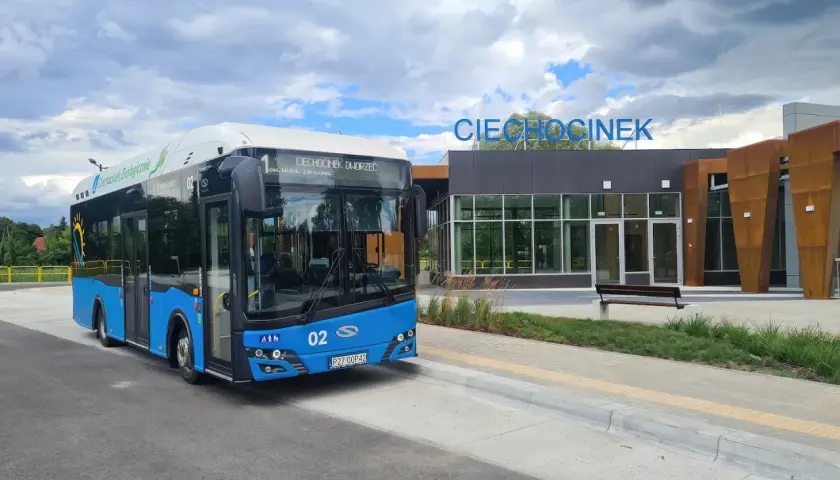 Niebieski autobus ekologiczny z napisem "Ciechocinek Dworzec" czeka na pasażerów. W tle nowoczesny budynek dworca z napisem "Ciechocinek".
