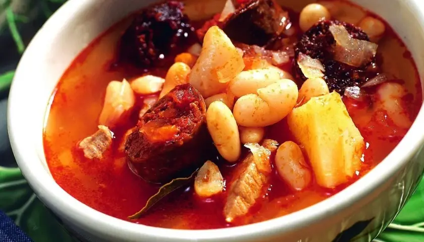 Un reconfortante plato de alubias con chorizo, trozos de patata y carne en un caldo rojizo.