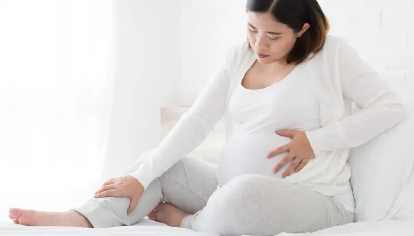 Schwangere Frau mit Hand auf dem Bauch und Bein, die Beschwerden oder Kompression während der Schwangerschaft andeutet.