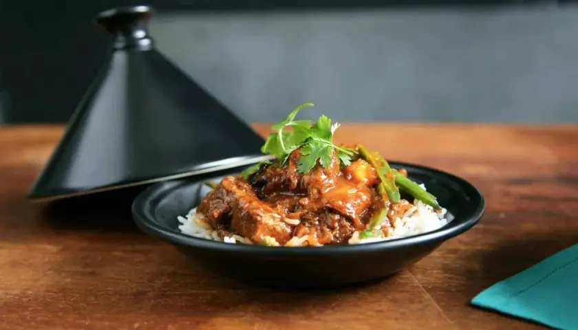Un plat de riz blanc garni d'un ragoût de bœuf savoureux, aux haricots verts et coriandre, servi à côté d'un tajine noir. La marinade boeuf a conféré une sauce riche et appétissante.