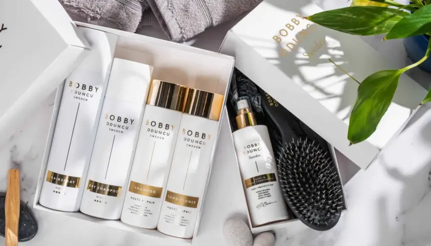 En presentbox med Bobby Oduncu-produkter för att ta hand om håret: hårspray, torrschampo, schampo, balsam och leave-in spray. En borste ligger bredvid.