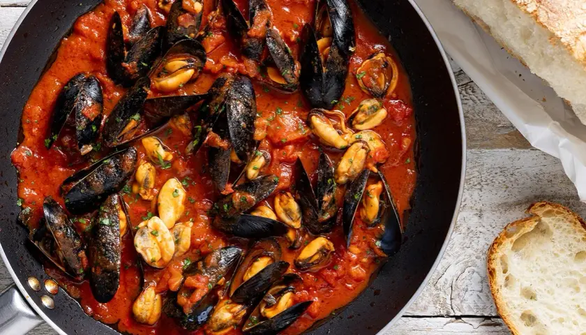 Cozze alla tarantina in padella, un piatto succulento con pane fresco a lato.