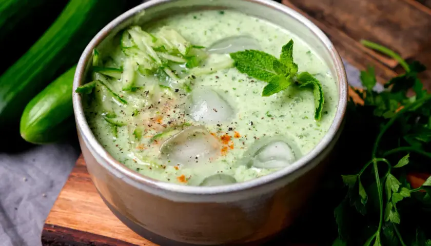 Erfrischende cremige kalte Gurkensuppe mit Eiswürfeln, Minze und geriebenen Gurken, garniert mit Pfeffer und Paprikapulver.
