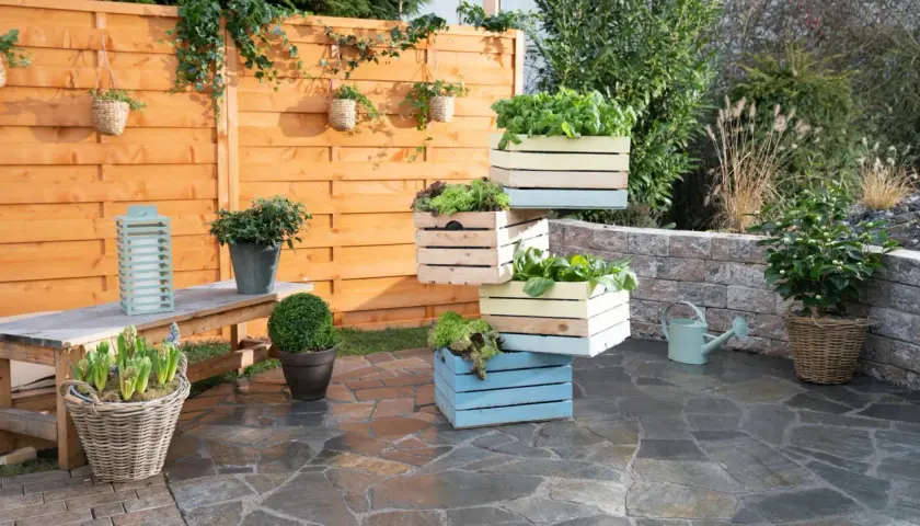 Fioriera fai da te con cassette di legno colorate, piene di verdure fresche, su un patio in pietra.