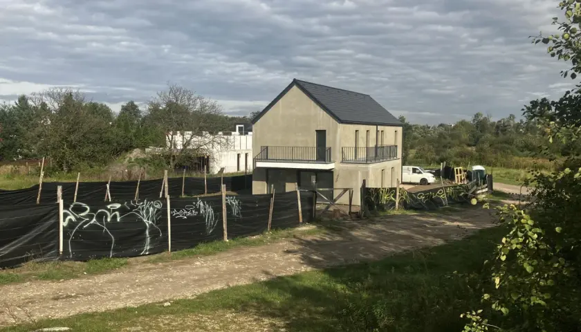 Plac budowy z niedokończonymi domami, ogrodzony czarną siatką z graffiti. Może to symbolizować zakaz budowy domów jednorodzinnych w tej okolicy.