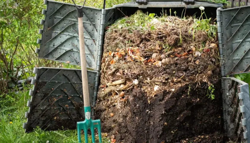 Przydomowy kompostownik pełen resztek organicznych, obok widły. To miejsce, gdzie powstaje cenny nawóz, a nie tylko odpady.