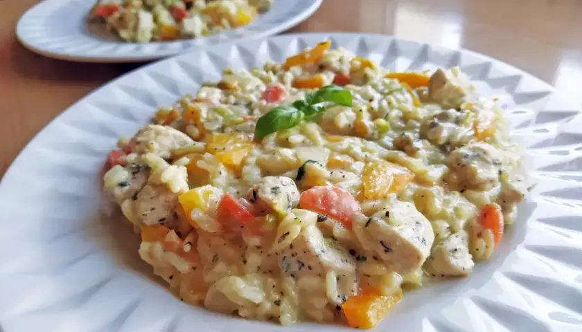 Szybkie risotto z kurczakiem i kolorowymi warzywami, ozdobione listkiem bazylii. Idealne na szybki obiad.