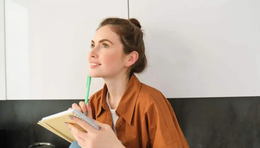 Ragazza pensosa, con un quaderno e una penna, dallo sguardo sognante. Una persona curiosa e operosa.
