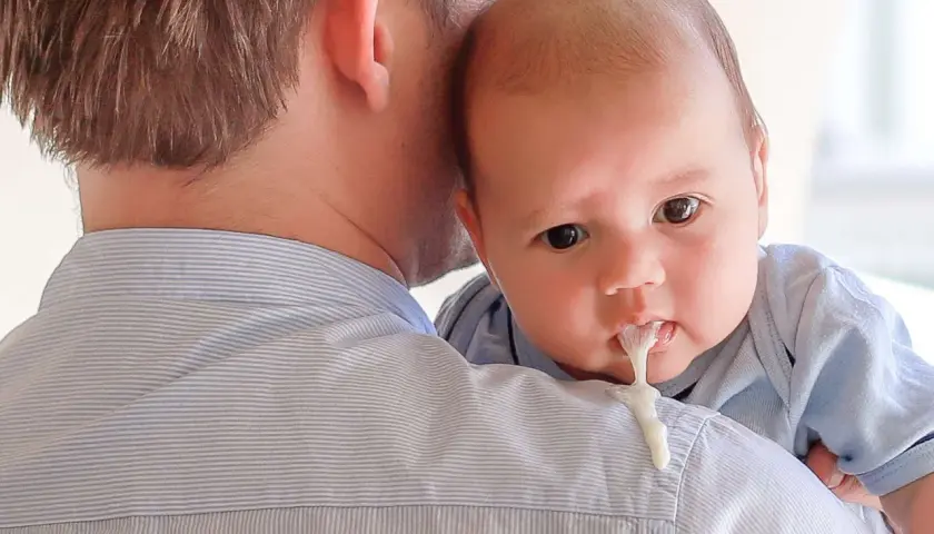 Neonato allattato al seno con reflusso, rigurgita latte sul pigiama del papà.