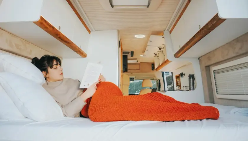 Une femme lit un livre, confortablement installée dans son camping-car fraîchement rénové. L'espace est lumineux et moderne.