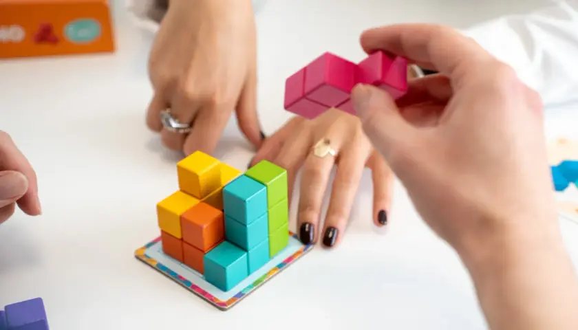 Mani che assemblano blocchi colorati, un gioco che stimola l'alto potenziale cognitivo.