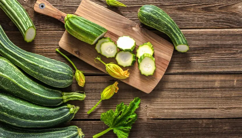 Frische Zucchini, einige roh geschnitten, liegen auf einem Holzbrett. Perfekt, um Zucchini roh zu essen!