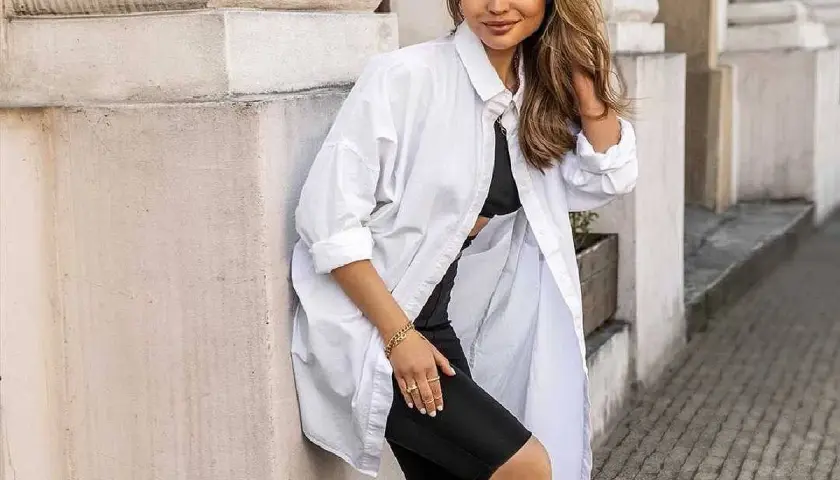 Kobieta w luźnej, białej koszuli i czarnych szortach kolarkach. Inspiracja na stylizacje z białą koszulą.
