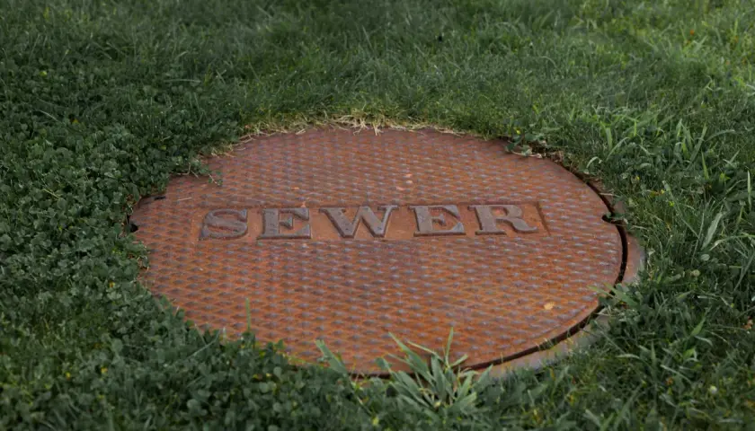 Zardzewiała pokrywa szamba z napisem "SEWER" w trawie. Czy na szambo trzeba mieć pozwolenie?