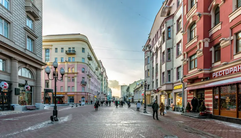 Zimowy spacer po Arbat w Moskwie. Ludzie przechadzają się brukowaną ulicą między kolorowymi kamienicami, a w oknach sklepów migoczą świąteczne dekoracje.