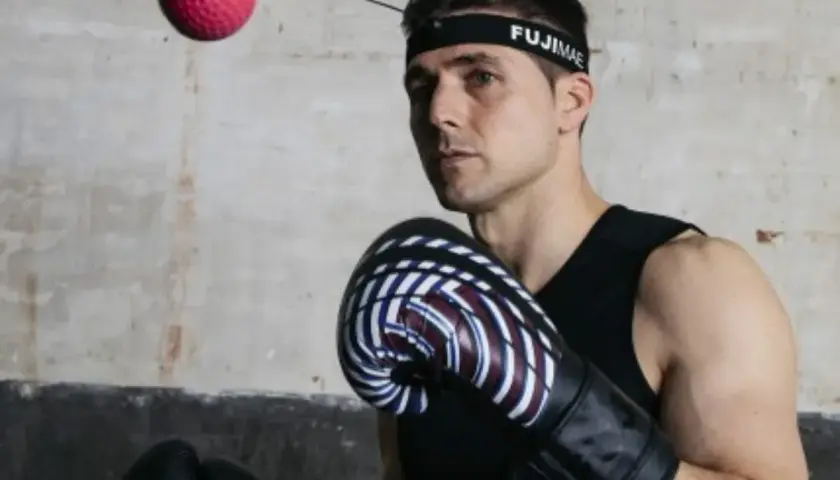 Bokser w rękawicach i opasce FUJIMAE, japoński producent sprzętu sportowego, ćwiczy z piłką refleksyjną.