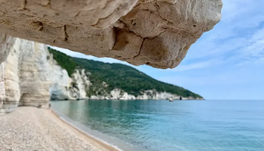 Vue depuis une grotte sur une plage de galets, mer turquoise et falaises blanches sur la côte adriatique Italie.