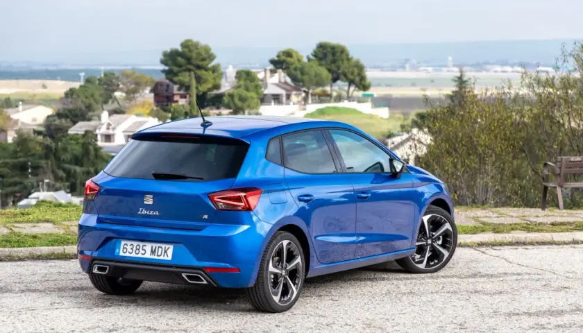 Un Seat Ibiza 1.2 gasolina, azul brillante, aparcado en un paisaje con casas y árboles. Opiniones sobre su diseño y rendimiento.