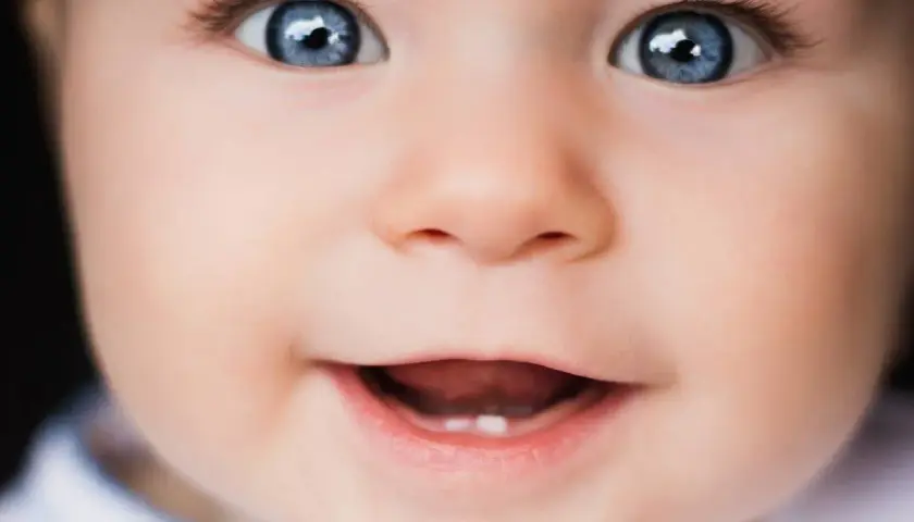 Occhi azzurri e un sorriso che mostra il primo dentino. Una bellissima vista neonati che incanta.