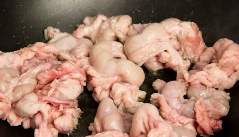 Unos gallinejas y entresijos crudos se cocinan en una sartén negra, listos para ser un plato tradicional.